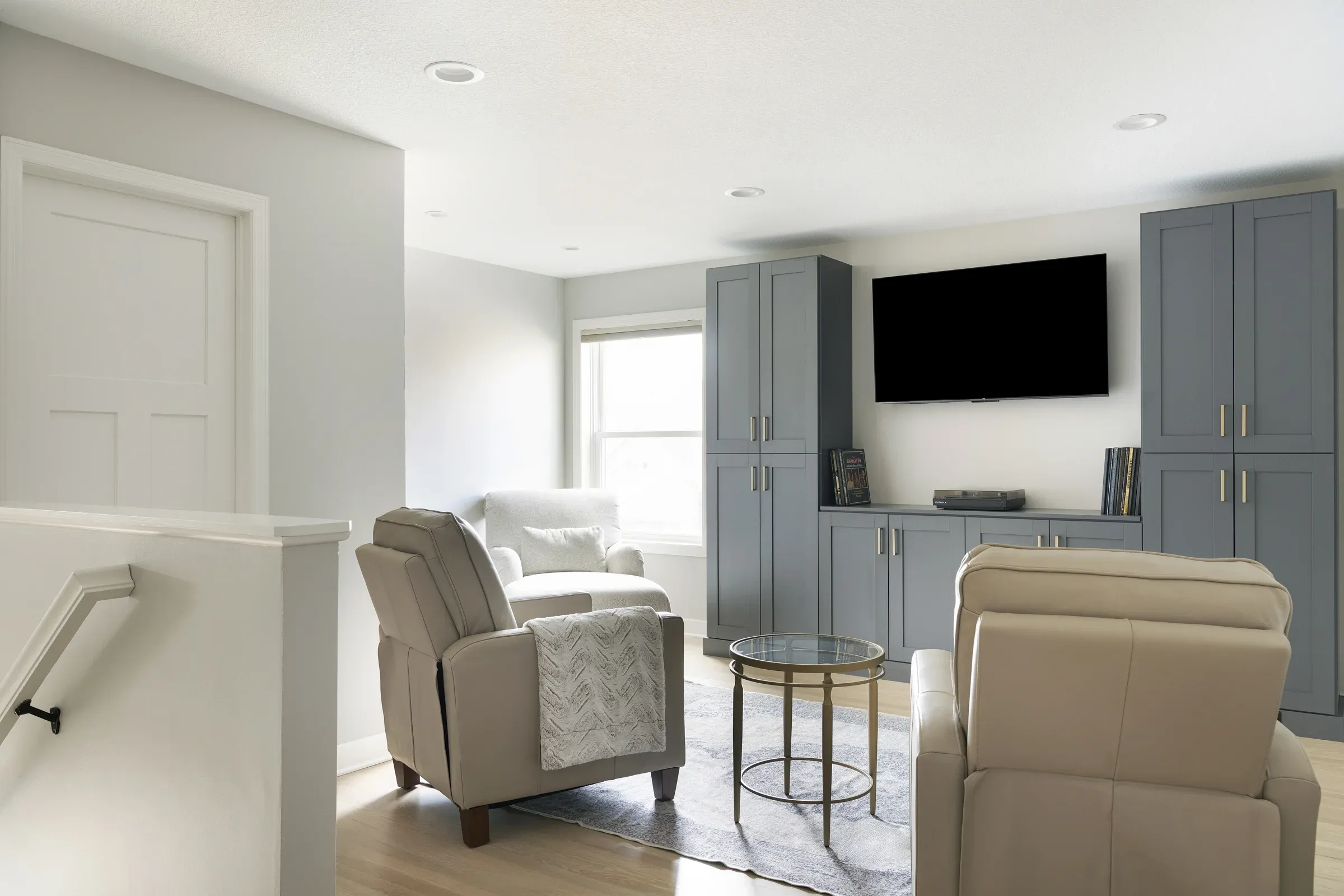 Second-floor entertainment loft with hardwood flooring, blue-gray cabinet storage wall, wall-mounted TV, and recessed lighting – Elko New Market whole-home remodel by Honey-Doers Remodeling